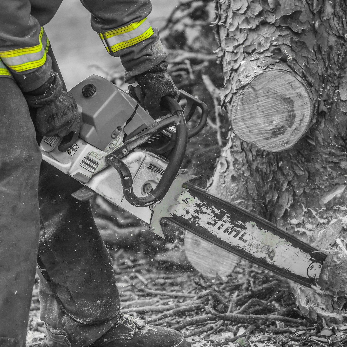 An emergency worker uses a chainsaw to clear a fallen tree during an incident.
