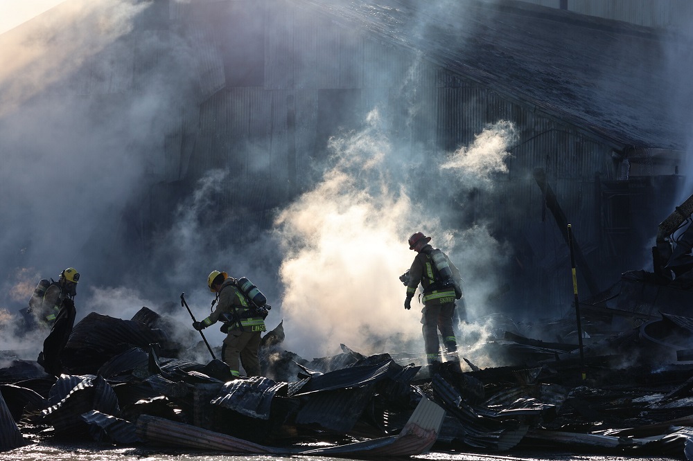 Three CAL FIRE firefighters pick through the wreckage of a burned out industrial building