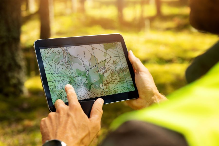 A man holds a tablet displaying an interactive topographic map