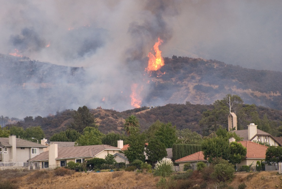 Houses sit in the foreground of a burning hillside